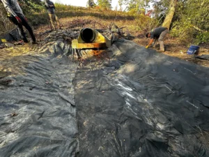 A close-up view of a riprap apron with loose stones around a culvert outlet, designed to slow stormwater flow and prevent erosion in a natural setting.